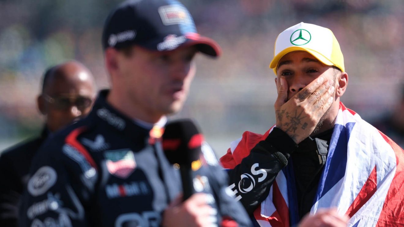 Lewis Hamilton stands behind Max Verstappen as he gives his post-race interview