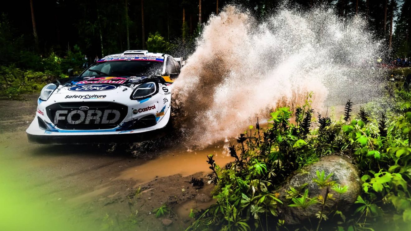 A Ford Puma Rally1 car splashes spectacularly through a puddle during the 2024 Rally Finland
