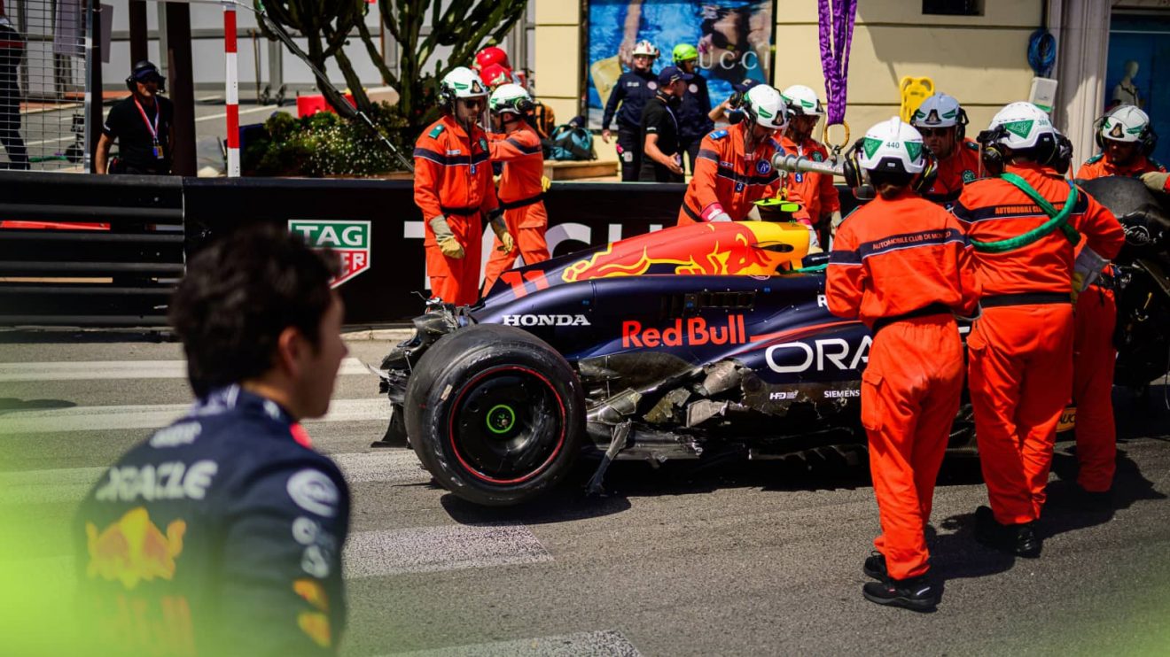 A group of marshals tend to a severely damaged Red Bull in Monaco as Sergio Perez looks on in the foreground
