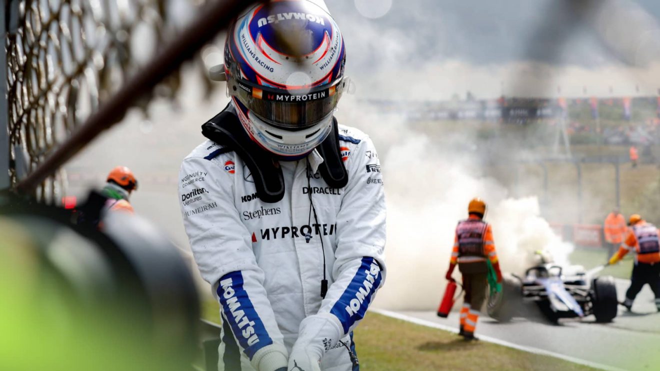 Logan Sargeant bows his head as he removes his gloves and walks away from the wreckage of his Zandvoort crash, with his destroyed Williams tended to by marshals in the background