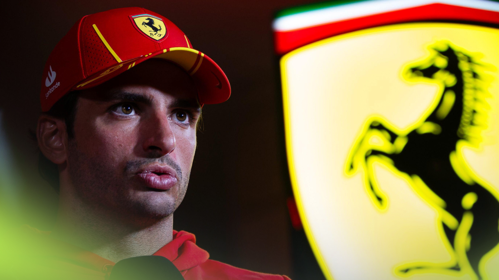 Carlos Sainz speaks in an interview with a large Ferrari logo in the background