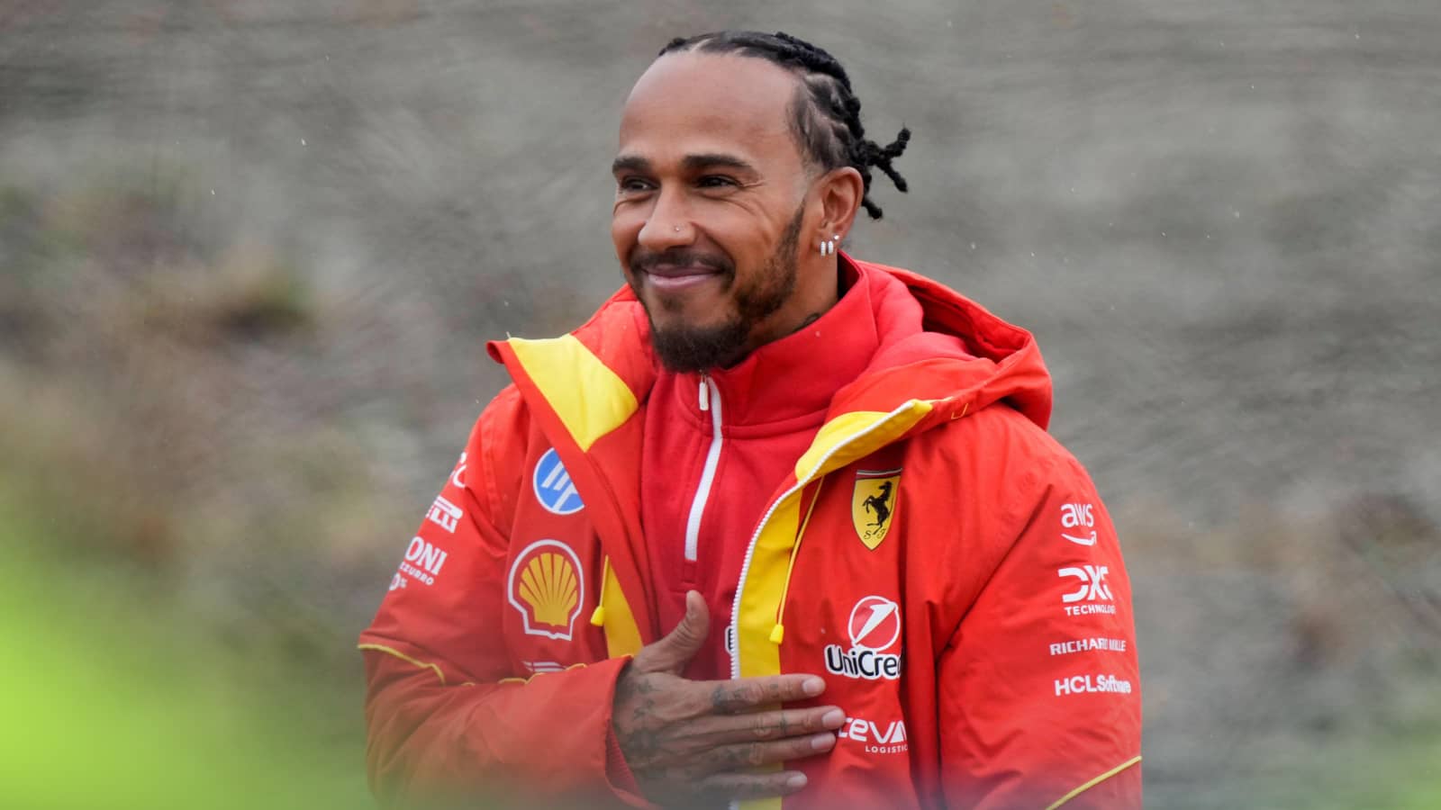 Lewis Hamilton smiles and holds his hand to his chest as he greets fans at Fiorano while wearing a Ferrari team coat