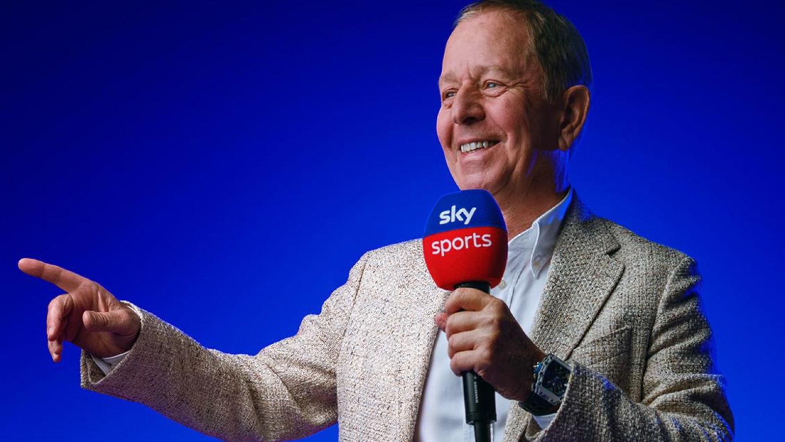 Sky F1 pundit and co-commentator Martin Brundle smiling and pointing while holding a Sky F1-branded microphone