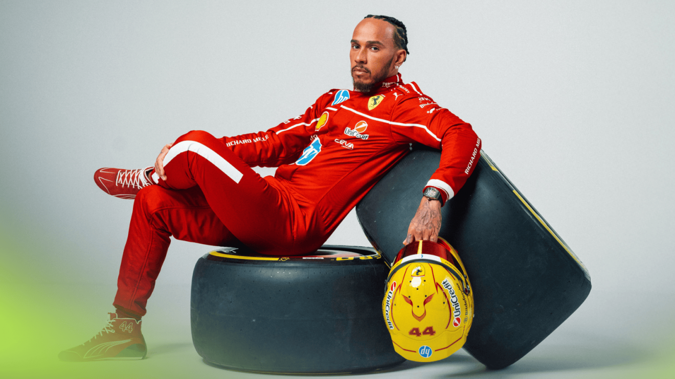 A studio shot of Lewis Hamilton sitting on some tyres while wearing Ferrari overalls and holding his 2025 race helmet