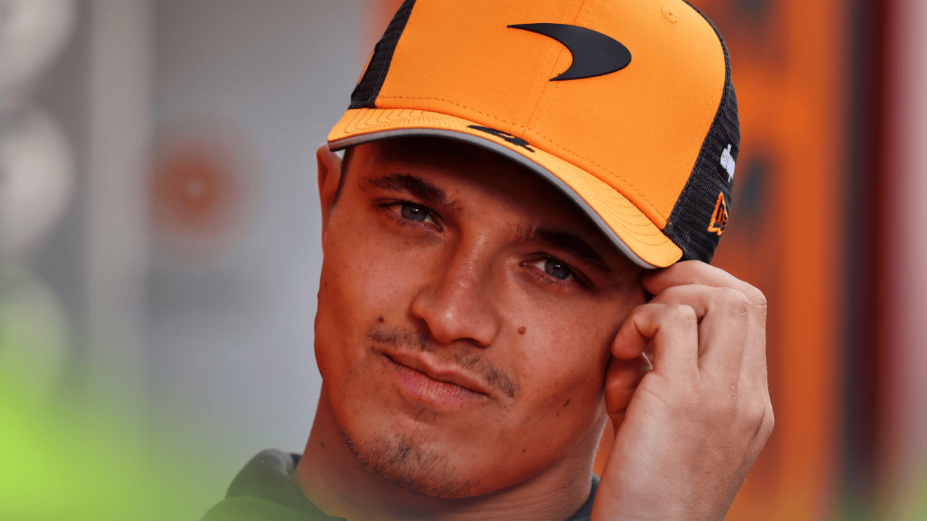 Lando Norris holds his hand to his head while wearing a McLaren cap