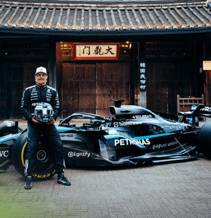 Valtteri Bottas holds his helmet as he sits on the tyre of a Mercedes W13 during a photocall