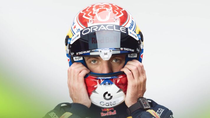 A studio shot of Max Verstappen adjusting his helmet with his visor open
