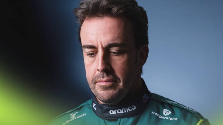 A studio shot of Fernando Alonso looking downwards while wearing Aston Martin overalls