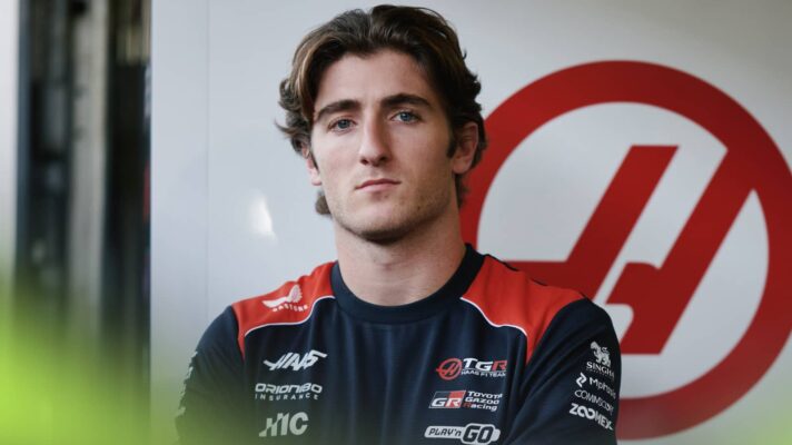 Jack Doohan eyes the camera as he poses alongside a Haas logo in the team's garage