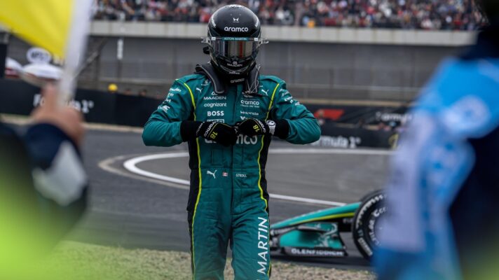 Lance Stroll wearing his full racing overalls and helmet takes his gloves off while walking away from his Aston Martin after retiring from the Chinese GP.