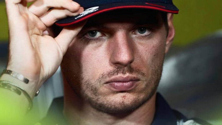 A close-up shot of Max Verstappen pinching the peak of his cap in a press conference
