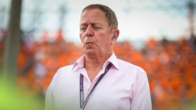 Martin Brundle stood against a fence on the grid in Hungary with fans wearing orange in the background