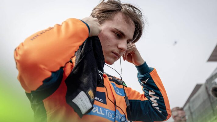 Oscar Piastri inserts his earplugs on the grid with a grey sky above him
