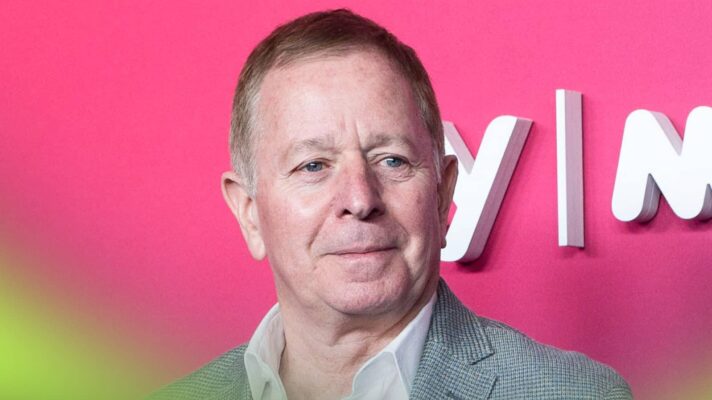 Martin Brundle smiles with a bright-pink board in the background