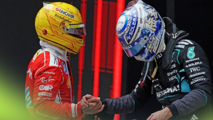 Lewis Hamilton and George Russell shake hands with the helmets on in parc ferme after climbing out of their cars.