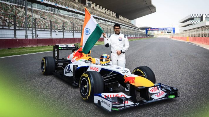 Karun Chandhok waves the flag of India while posing with an F1 car on the main straight at the Buddh International Circuit