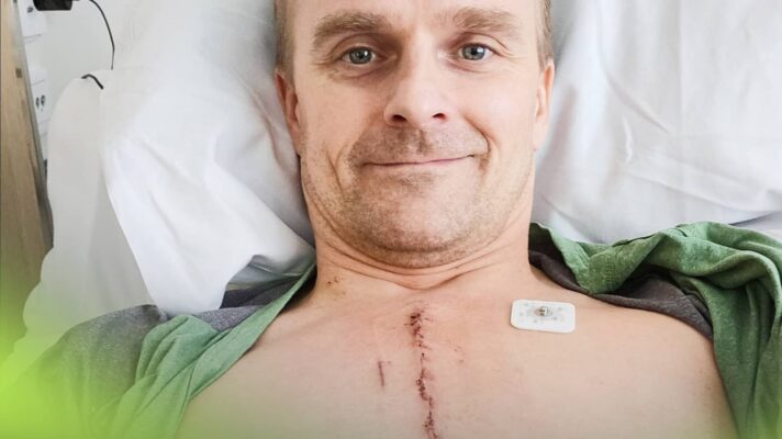 A selfie of Heikki Kovalainen lying in bed after open heart surgery with a large scar running down the middle of his chest