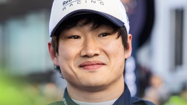 A close-up shot of Yuki Tsunoda smiling while wearing a Red Bull F1 cap and overalls