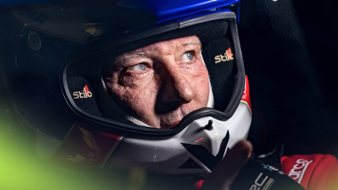 Jos Verstappen looks on in the darkness while wearing an open-faced rally helmet