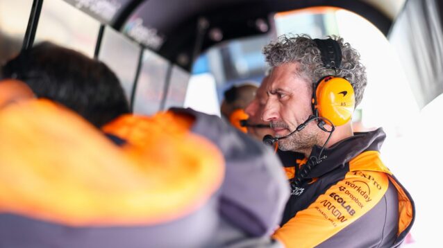 Andrea Stella sits on the pit wall, looking at data while wearing his McLaren headphones.