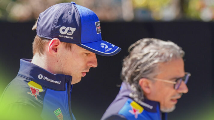 Max Verstappen walks through the paddock while, in the background, Laurent Mekies walks alongside, talking to him.