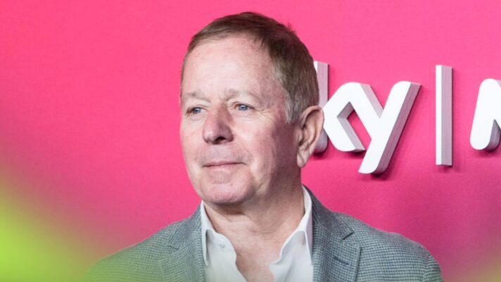 Martin Brundle looks on as he poses against a bright-pink background