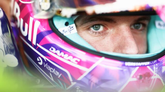 A close-up shot of Max Verstappen sitting in the cockpit of the Red Bull RB22 with the visor of his helmet open