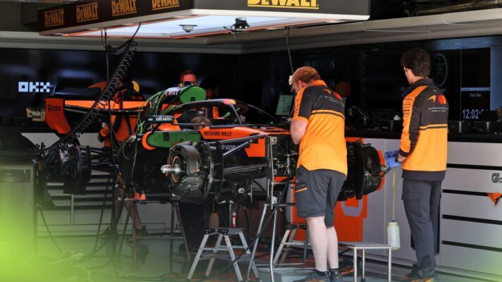 Mechanics in the McLaren garage work on the car on stands, with its nose, wheels, and sidepods dismantled.