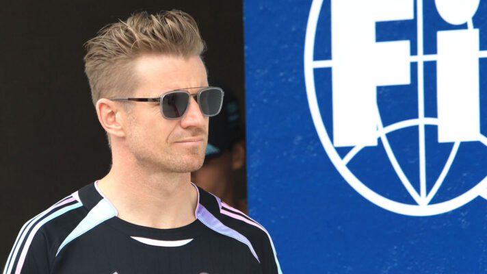 Nico Hulkenberg wearing sunglasses and an Audi branded top as he walks past an FIA logo