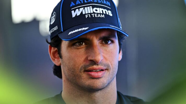 Carlos Sainz looks on while wearing a Williams team cap in the paddock
