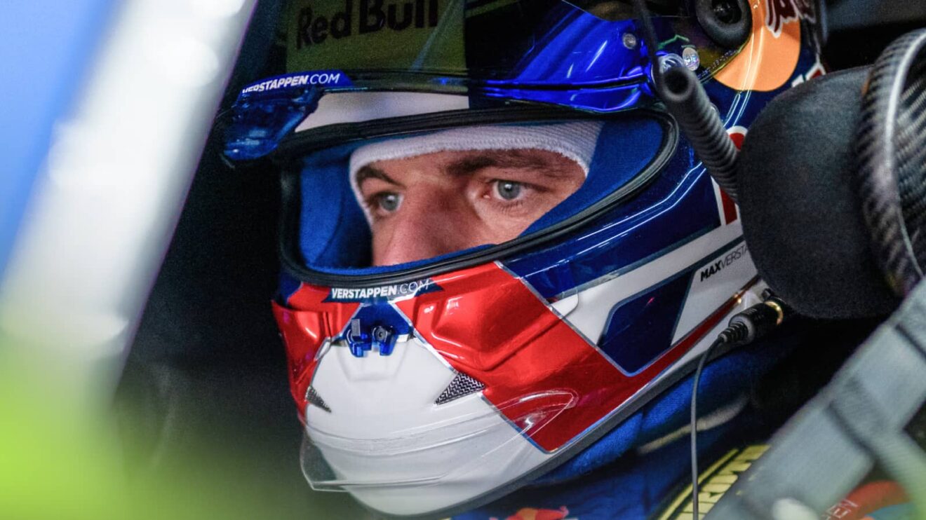 A close-up shot of Max Verstappen sitting in the cockpit of his Mercedes-AMG GT3 with the visor of his helmet open