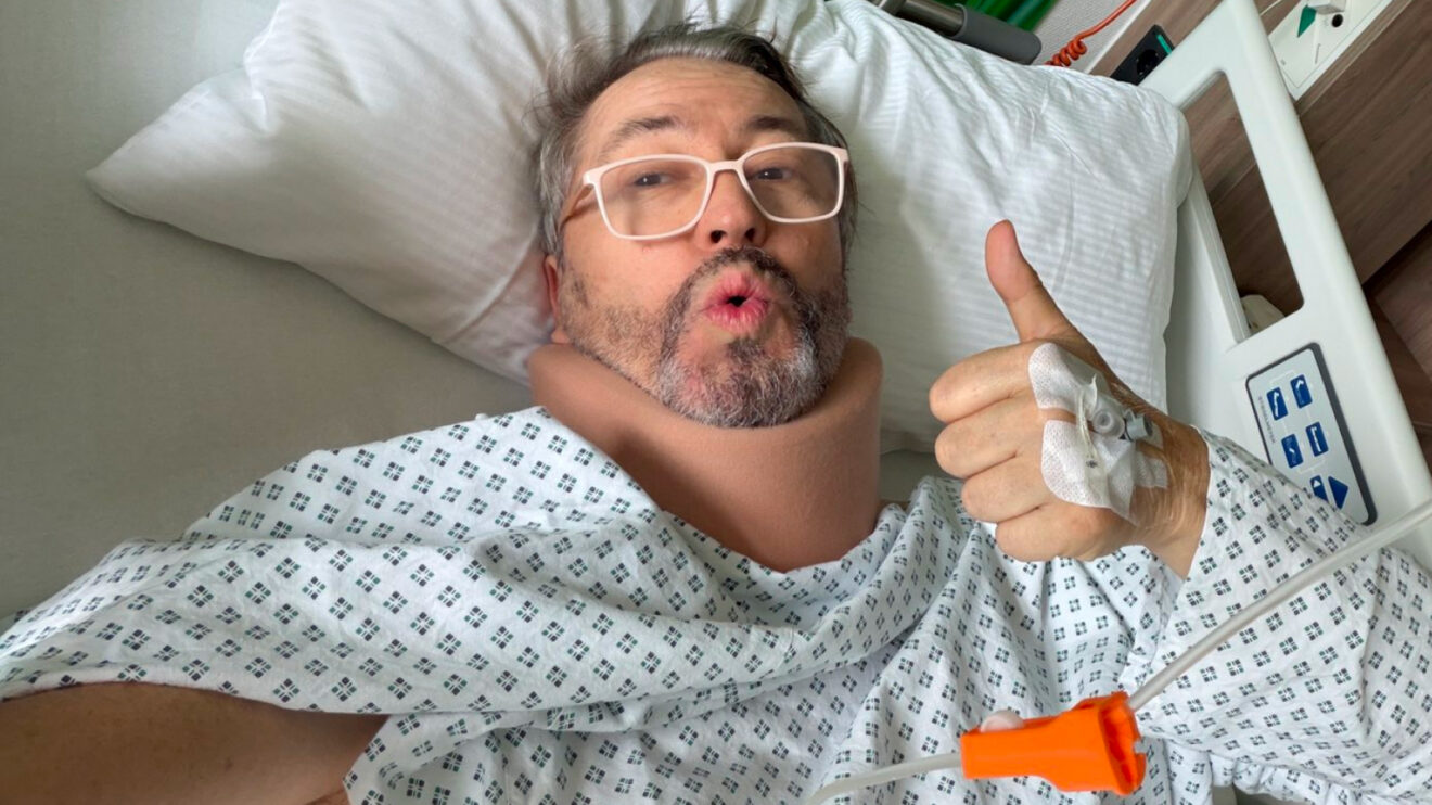 Heinz-Harald Frentzen gives a thumbs up as he lies on his back in a hospital bed while wearing a neck brace