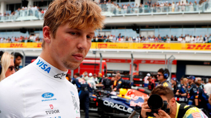 Liam Lawson walking on the grid with a photographer taking photos and a Red Bull in the background