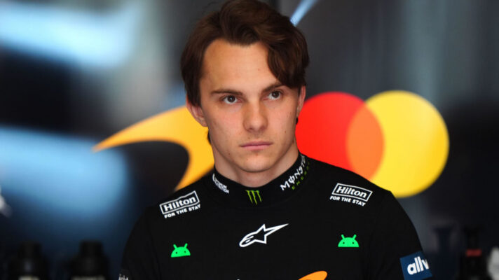 Oscar Piastri in the McLaren garage with the team's logo and the Mastercard logo on the wall behind him