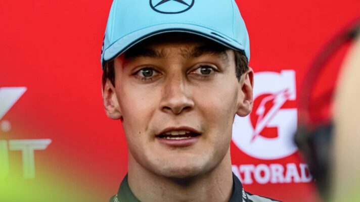 George Russell speaks to the media against a red background