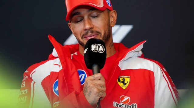 Lewis Hamilton shuts his eyes as he holds an FIA-branded microphone in a press conference