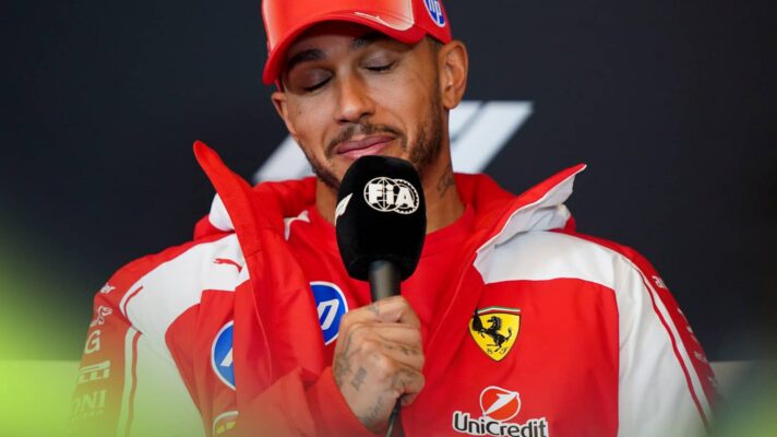 Lewis Hamilton shuts his eyes as he holds an FIA-branded microphone in a press conference