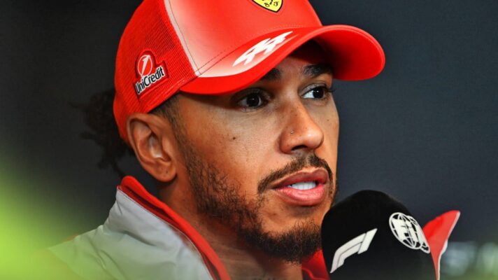 A close-up shot of Lewis Hamilton speaking into a microphone at a press conference
