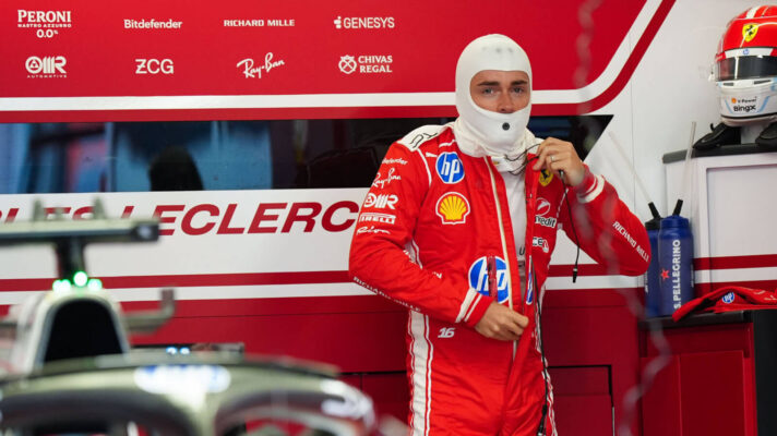 Charles Leclerc doing up his race suit in the back of the Ferrari garage, car's Halo in the foreground