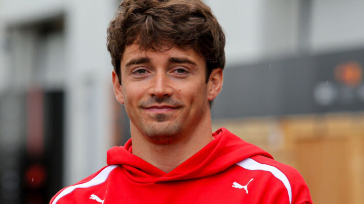 Charles Leclerc smiling as he stands in front of the camera in a Ferrari hoodie
