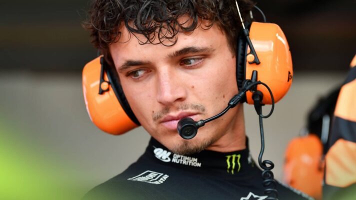 Lando Norris looks downwards while wearing a set of McLaren headphones