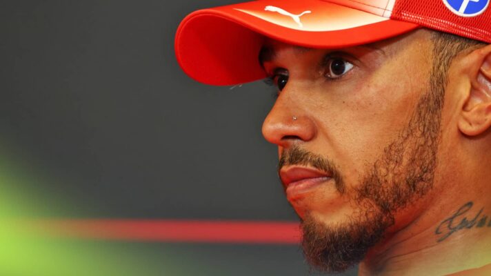 A close-up shot of Lewis Hamilton wearing a Ferrari cap in a press conference