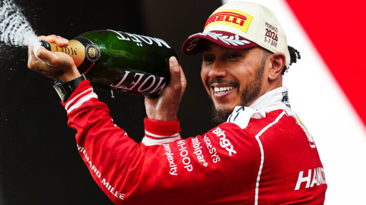 Lewis Hamilton smiling as he sprays the champagne on the podium in his Ferrari race suit