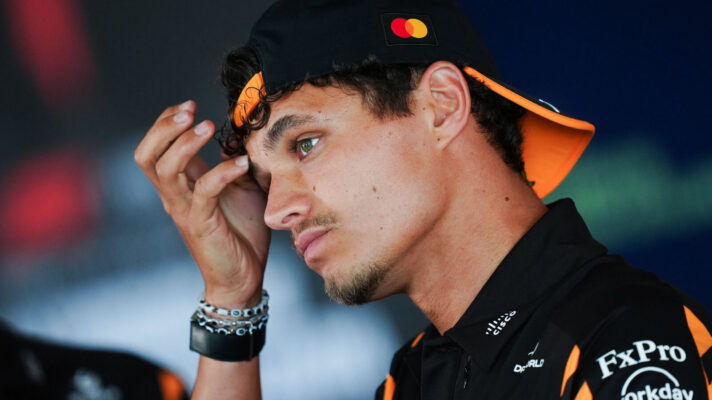 Lando Norris with his hand to his head during an interview, McLaren cap backwards