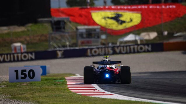 Lewis Hamilton on track in the Ferrari SF-26, huge Ferrari flag on the grass ahead of him