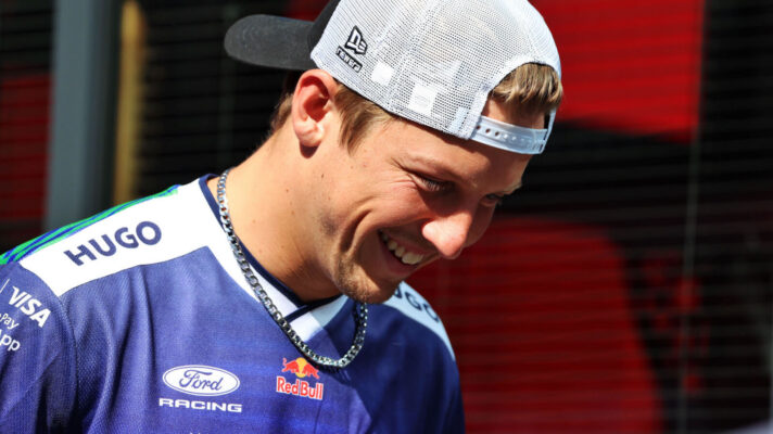 Liam Lawson laughing with his cap on backwards and his head down