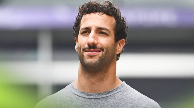 Daniel Ricciardo smiles thinly while wearing a grey t-short in the paddock
