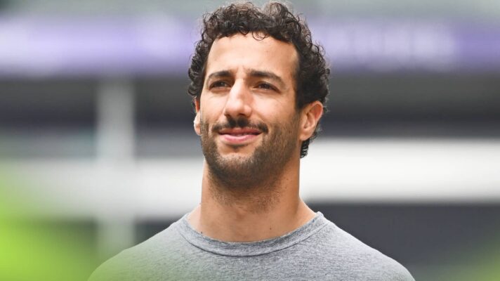 Daniel Ricciardo smiles thinly while wearing a grey t-short in the paddock