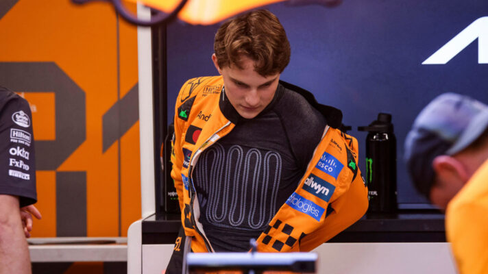 Oscar Piastri leaning over the rear wing of his McLaren wearing a cooling vest
