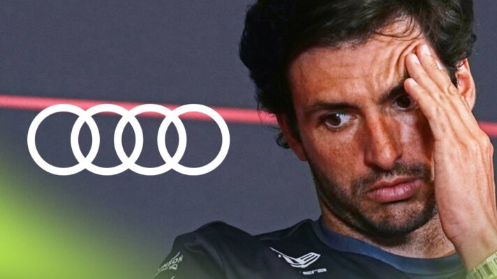Carlos Sainz presses his hand against his face in a press conference with a prominent Audi logo alongside him